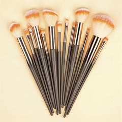 A 10-piece makeup brush set with dark gray handles, shiny silver ferrules, and soft bristles in white and light peach, arranged in a fan shape on a light beige background.