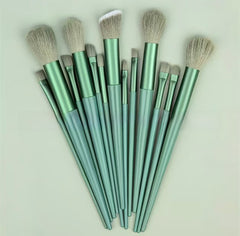 A set of ten makeup brushes with metallic sage green handles and light beige bristles, arranged in a fan shape on a light off-white background.
